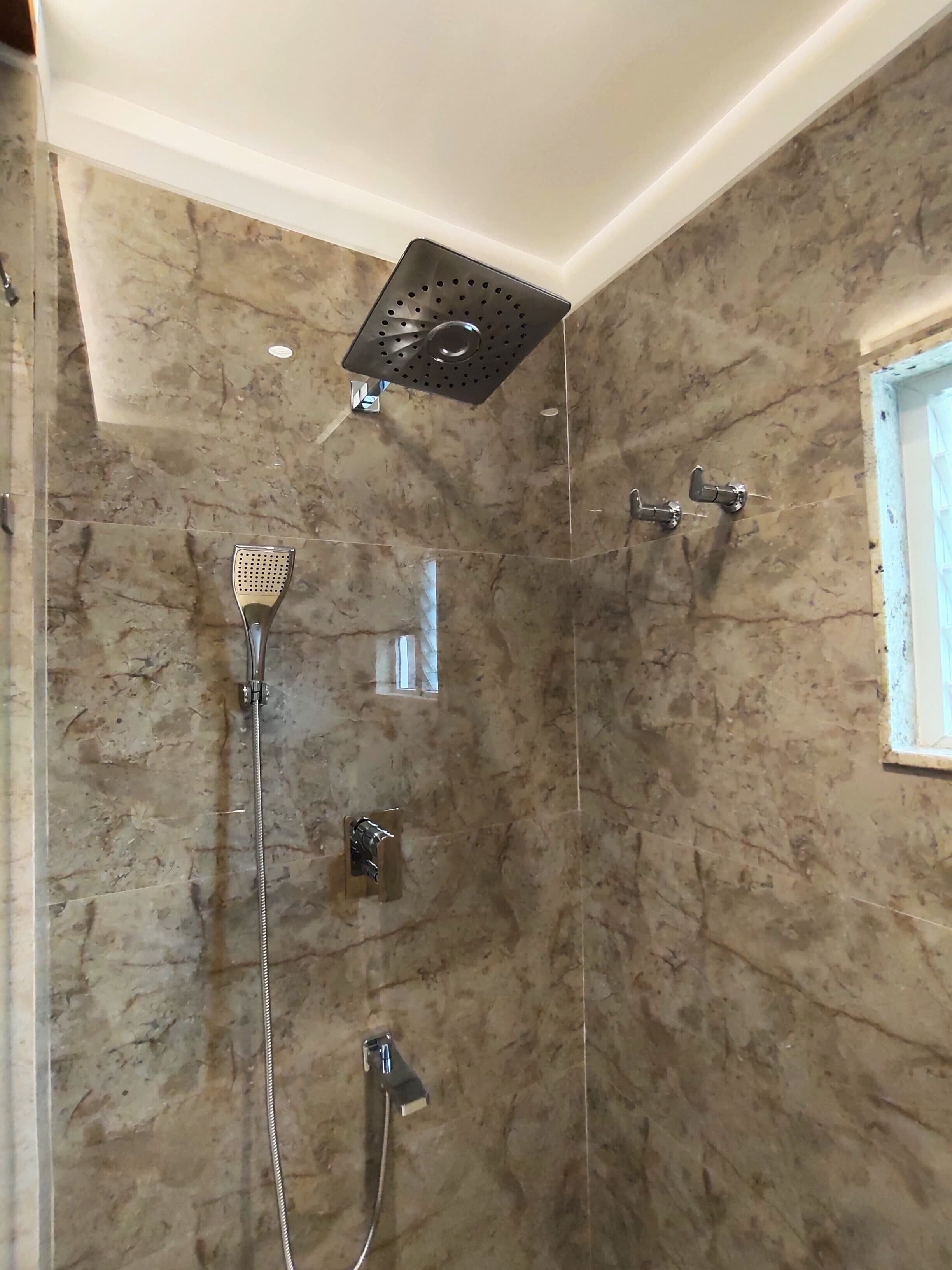 Une douche moderne dotée d’un pommeau de douche carré à effet pluie, d’un pommeau de douche à main et d’un robinet mural.