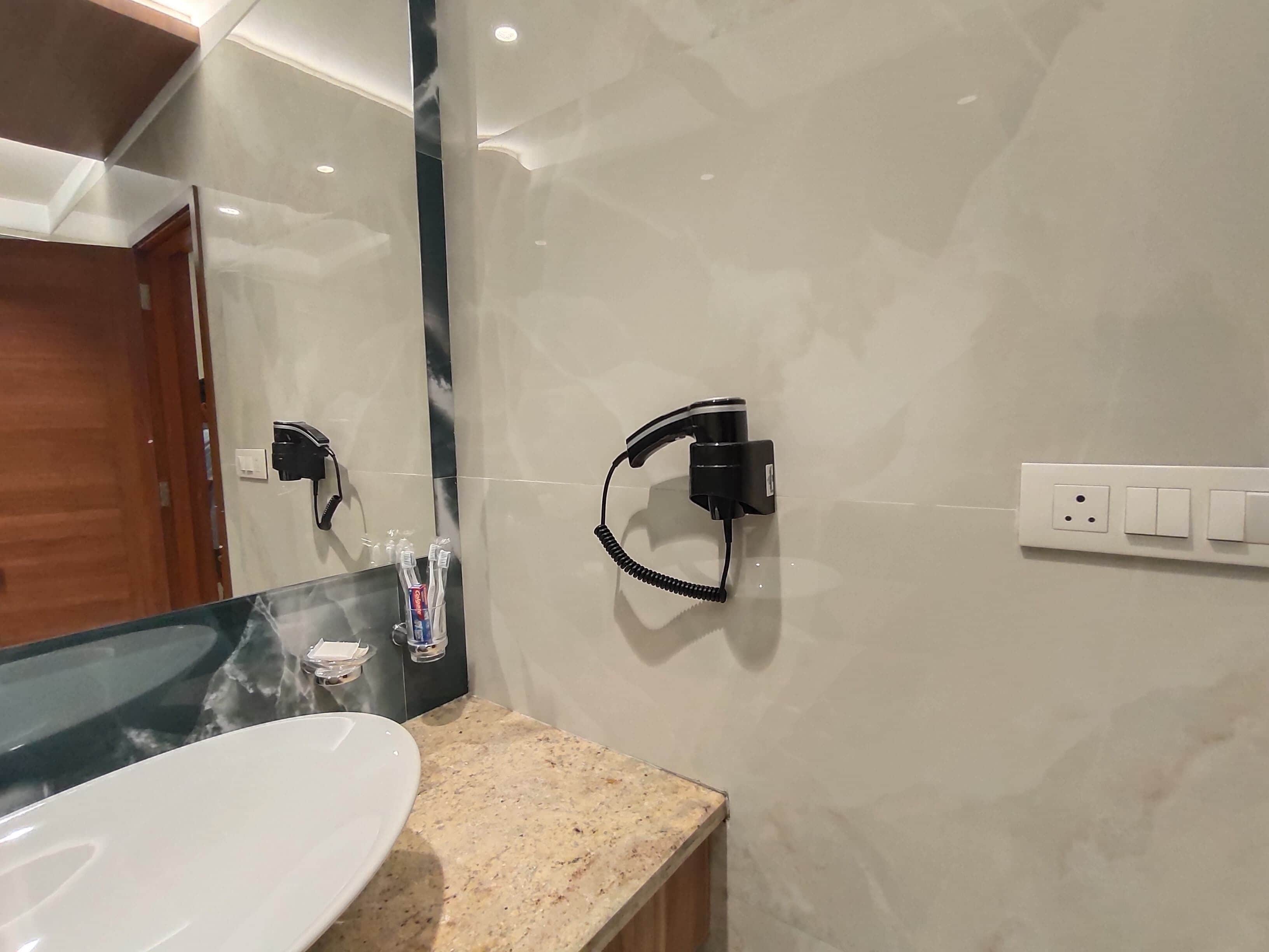 A bathroom with a white sink, a mirror, a towel rack, and a wall-mounted power outlet.