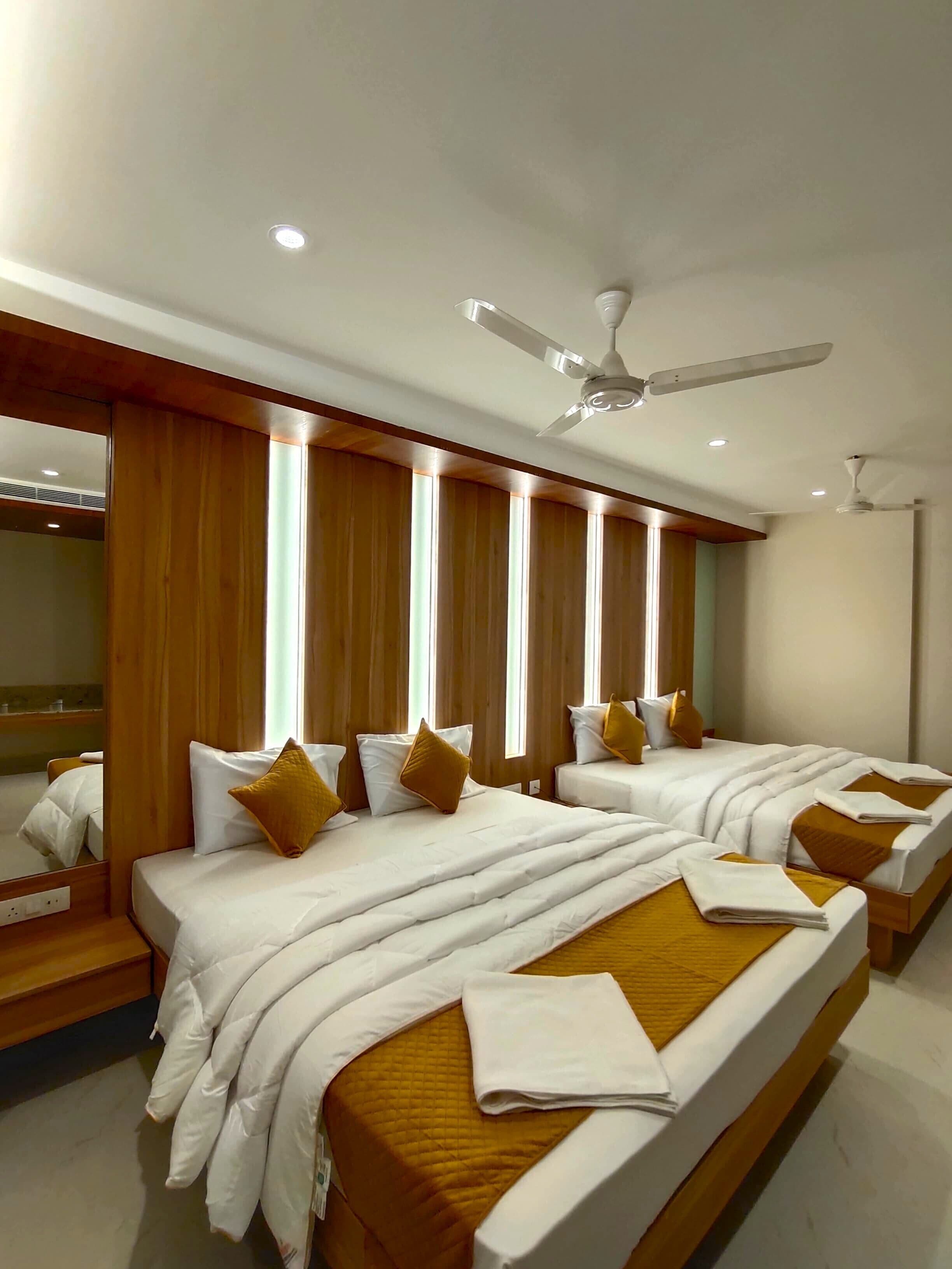 Una habitación de hotel con dos camas, paneles de madera, un ventilador de techo y un espejo grande.