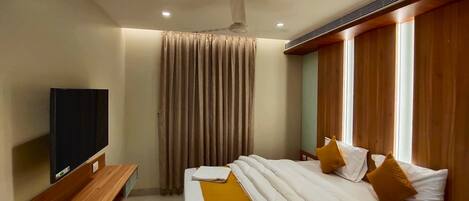 A hotel room with a bed, a TV, a wooden bench, and a window with curtains.