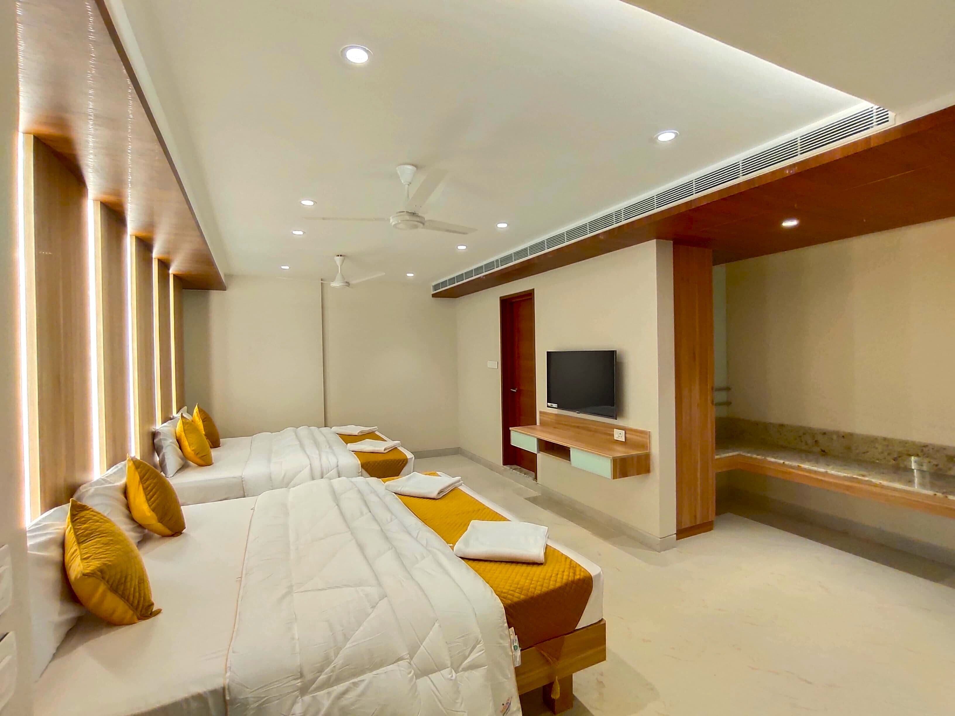 A hotel room with two beds, a TV, ceiling fans, and recessed lighting.