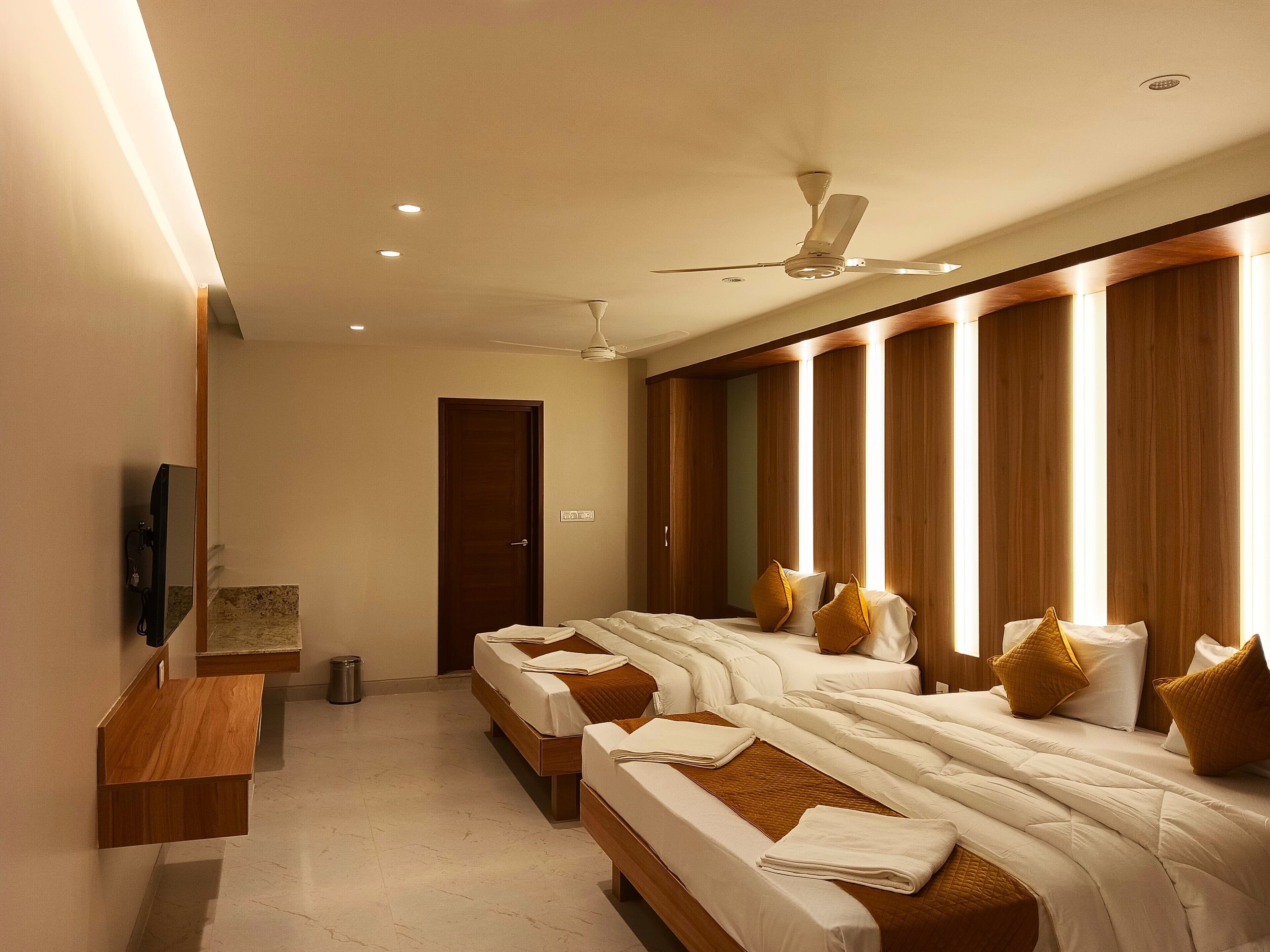 A hotel room with two beds, a ceiling fan, a TV, and a wooden bench.