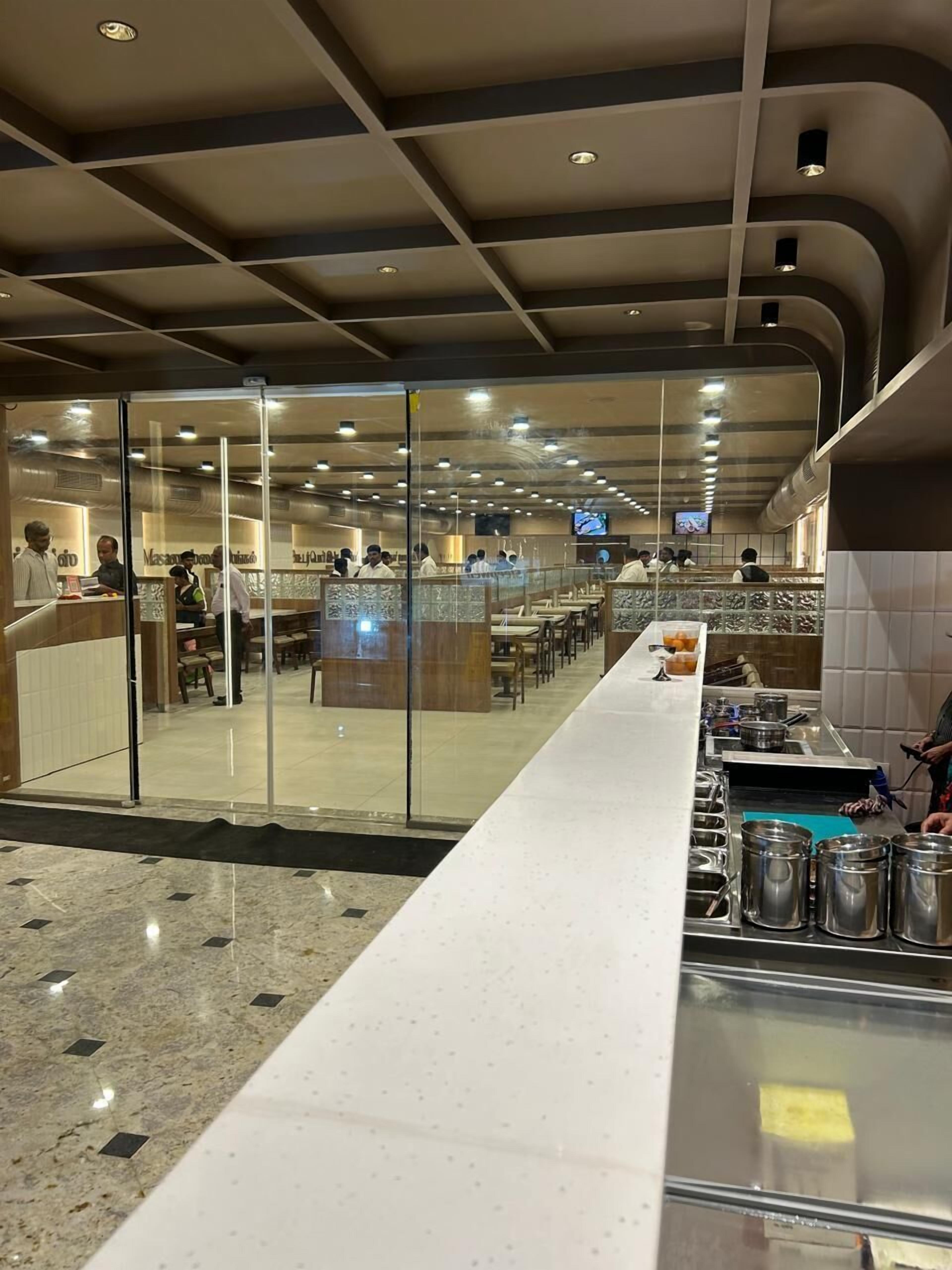 A modern restaurant with a long counter, glass partitions, and a tiled floor.