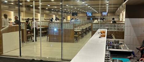 A modern restaurant with a long counter, glass partitions, and a tiled floor.