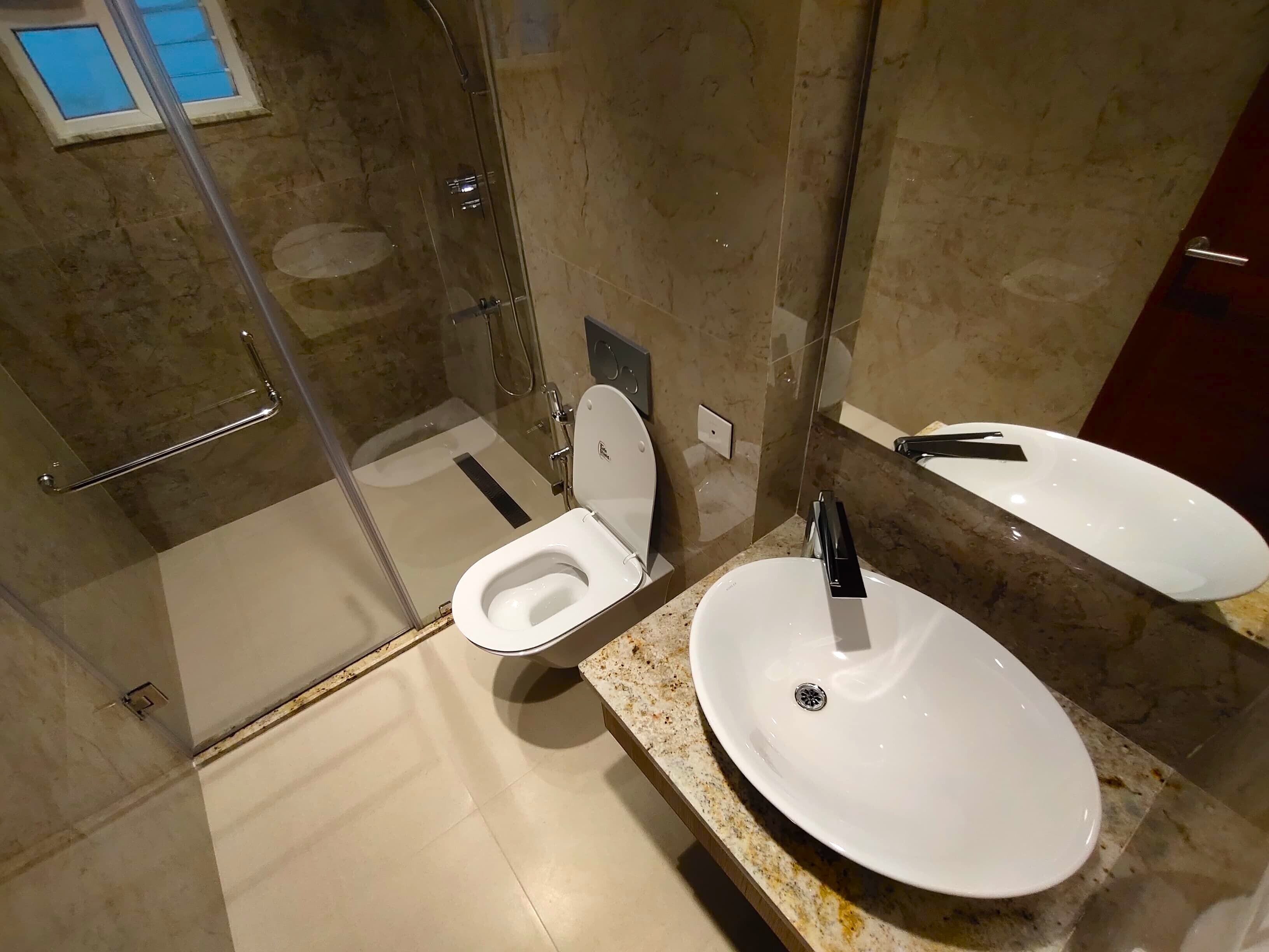 A modern bathroom with a glass-enclosed shower, a toilet, and two sinks with mirrors.