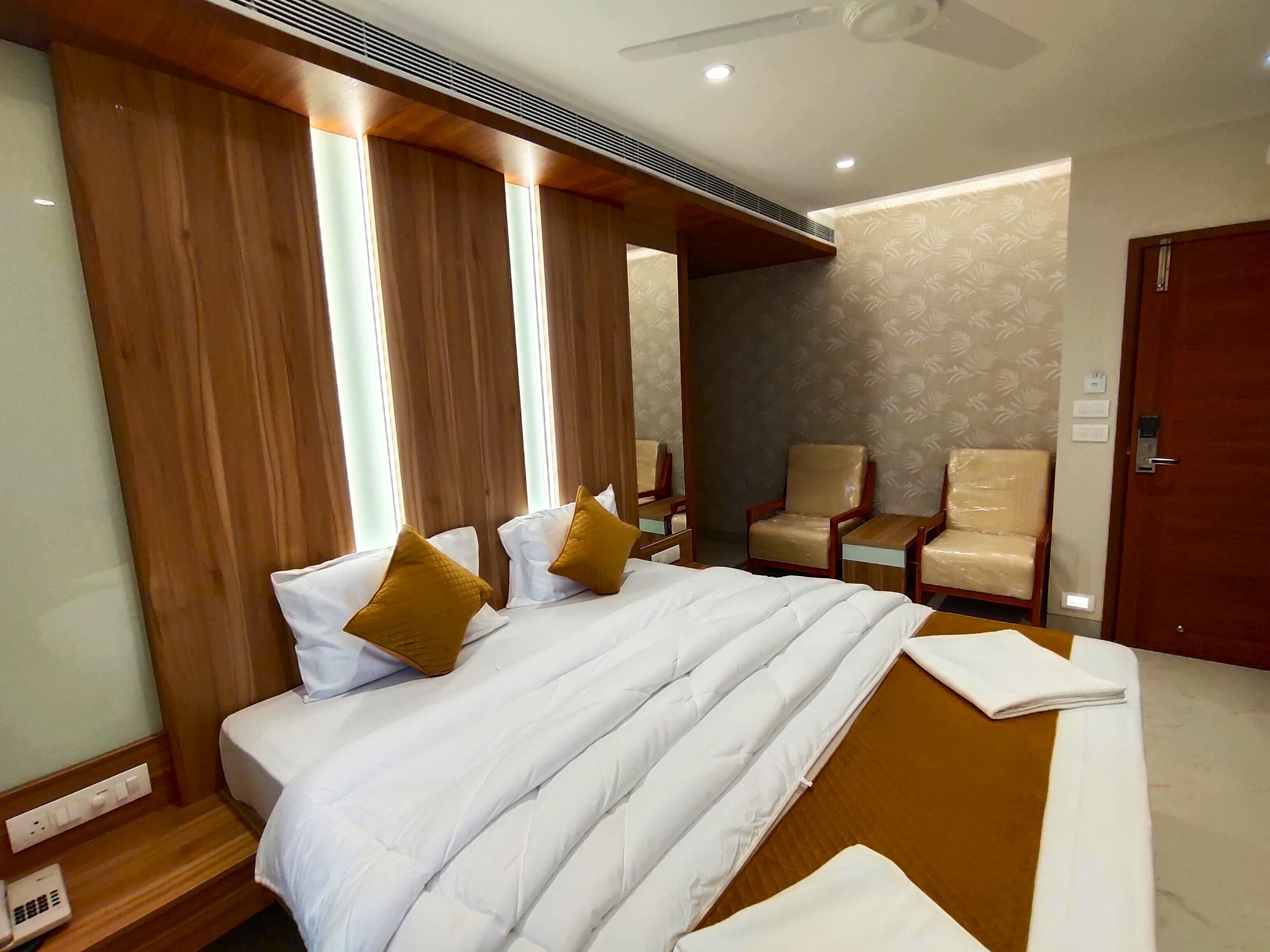 A hotel room with a large bed, two armchairs, a wooden headboard, and a ceiling fan.