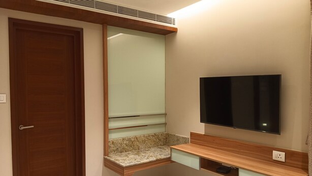 A bathroom with a wooden door, a mirror, a built-in sink with a granite countertop, and a mounted TV. - THE PARADISE KINGDOM (Kanchipuram)