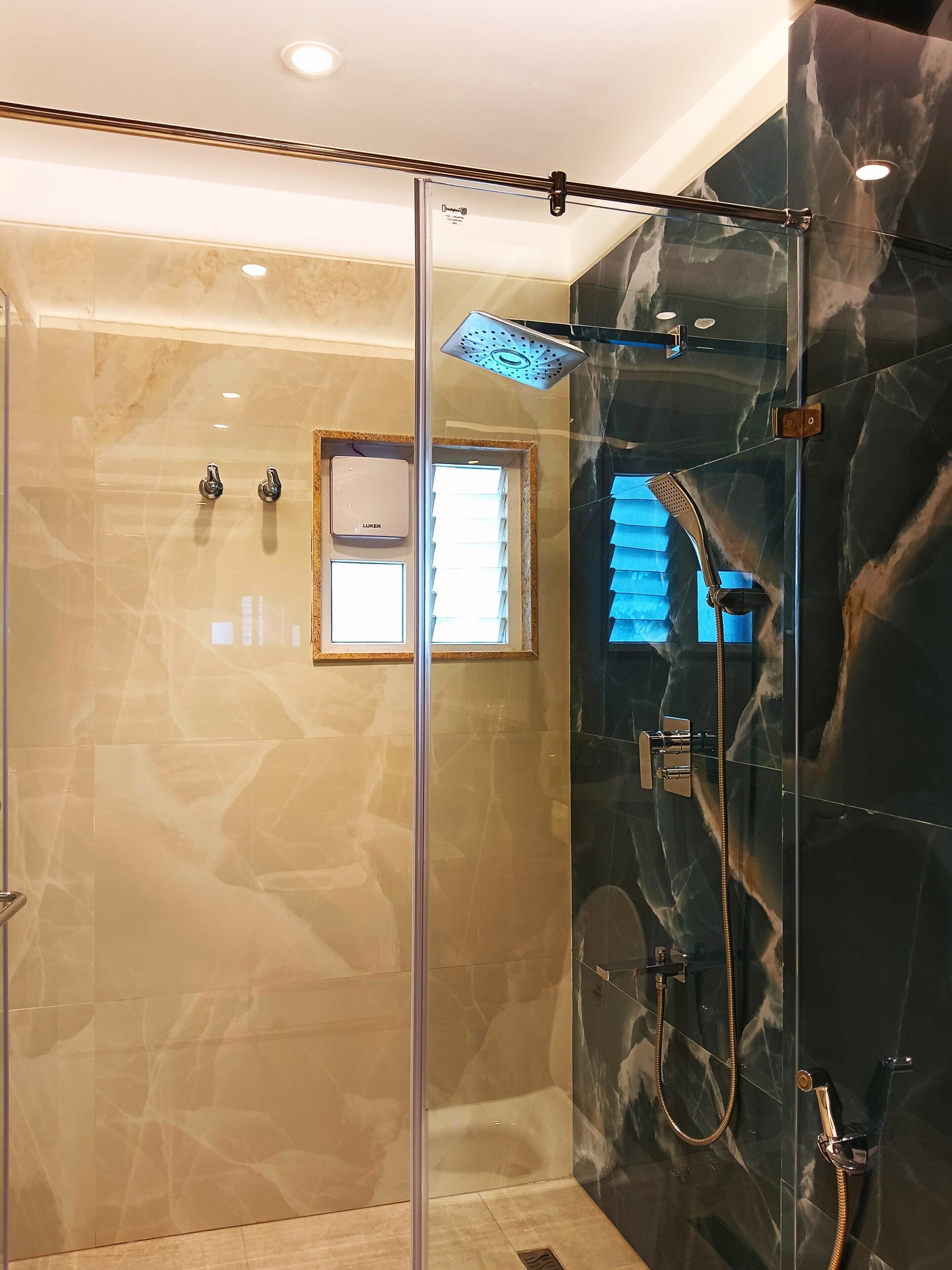 Un espace douche moderne doté d’une porte en verre, d’un pommeau de douche à main et d’un panneau de commande fixé au mur.