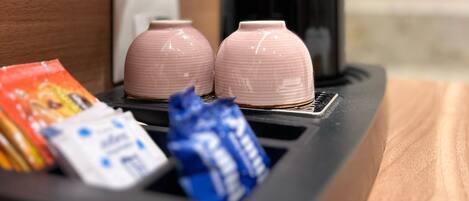 Un minibar con due tazze rosa in ceramica, una macchina da caffè nera e alcuni snack.