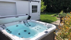 A hot tub with a wooden exterior, a white door, and a grassy yard with plants and a chair. - Cozy In Town Manchester Studio w/ Loft Bedroom. (Manchester)