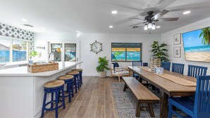 A modern kitchen with a large island, bar stools, and a view of the ocean through the windows. - Life can be a Beach (Gilbert)