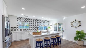 A modern kitchen with white cabinets, a large island with stools, a stainless steel refrigerator, and a decorative wall with star patterns. - Life can be a Beach (Gilbert)