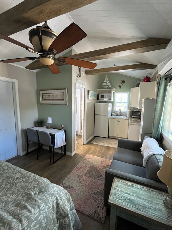 A compact room with a bed, a desk with a chair, a sofa, a ceiling fan, a kitchenette, and a window. - Charming studio with large outdoor patio. Fully fenced and pets are welcome! (St. Petersburg)