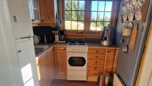 A compact kitchen with wooden cabinets, a stove, a sink, and a window with a view of trees. - Cozy cabin with a spectacular view! Pet-friendly - 15 minutes to skiing resort! (Buskerud)