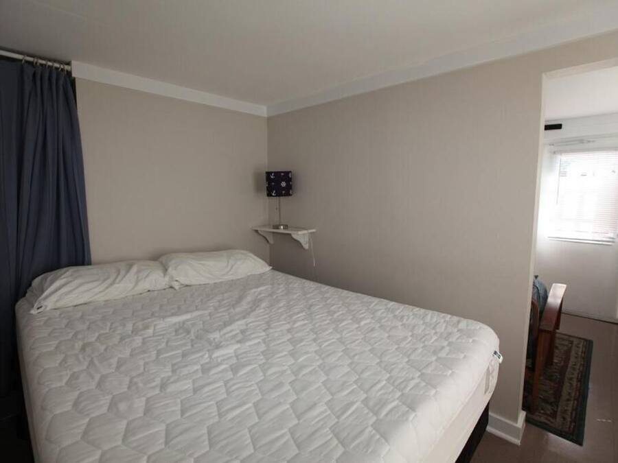 Een slaapkamer met een groot bed, een nachtkastje, een wandlamp en een deur naar een andere kamer.