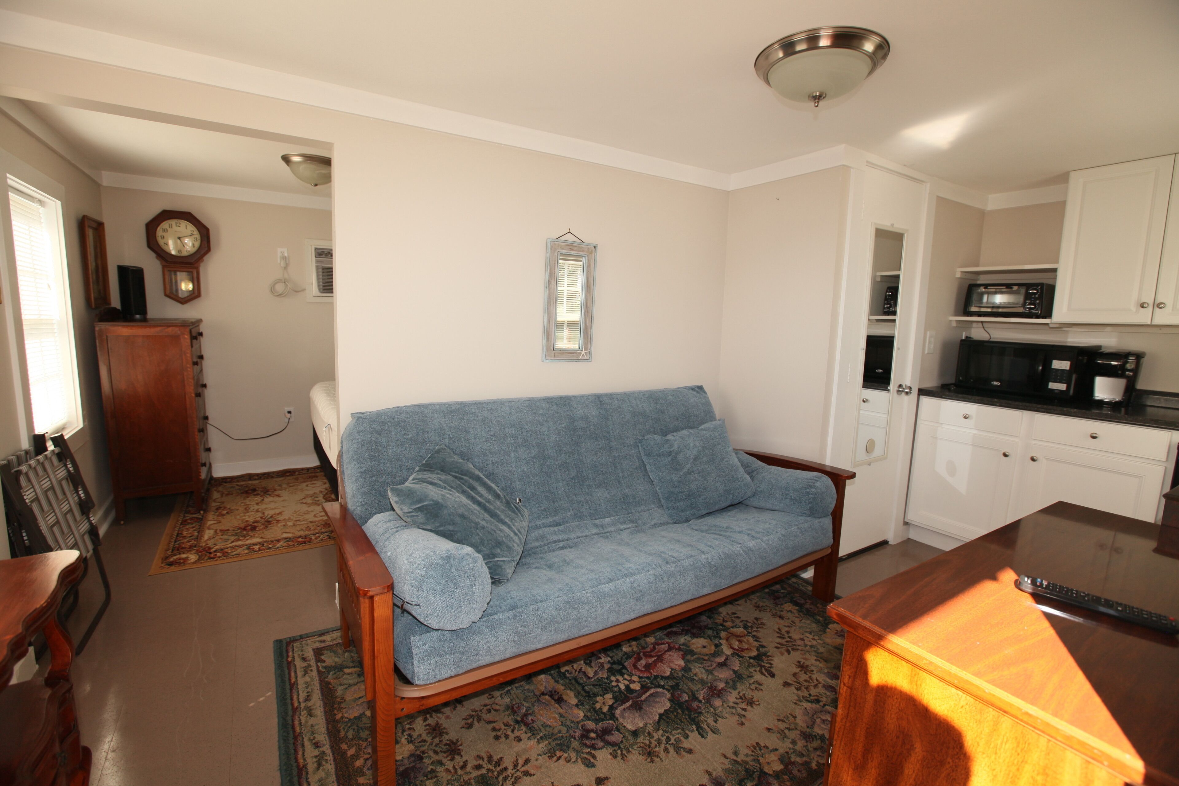 A living room with a blue sofa, a wooden coffee table, and a kitchen area with white cabinets and a microwave.