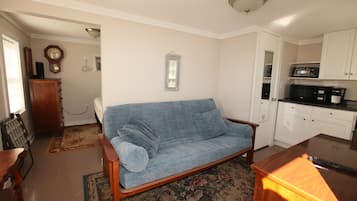 A living room with a blue sofa, a wooden coffee table, and a kitchen area with white cabinets and a microwave.