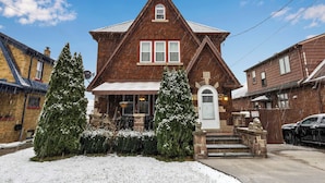 A two-story brick house with a steep gable roof, a front porch, and a snow-covered lawn.