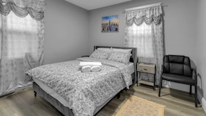 A bedroom with a bed, a chair, a nightstand, and a painting on the wall.
