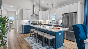 A modern kitchen with white cabinets, a stainless steel refrigerator, and a blue island with bar stools.