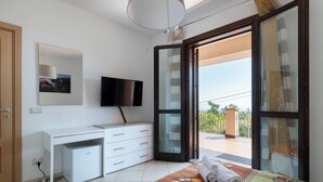 Habitación de hotel moderna con escritorio blanco, televisor de pantalla plana, refrigerador pequeño y balcón con vistas.