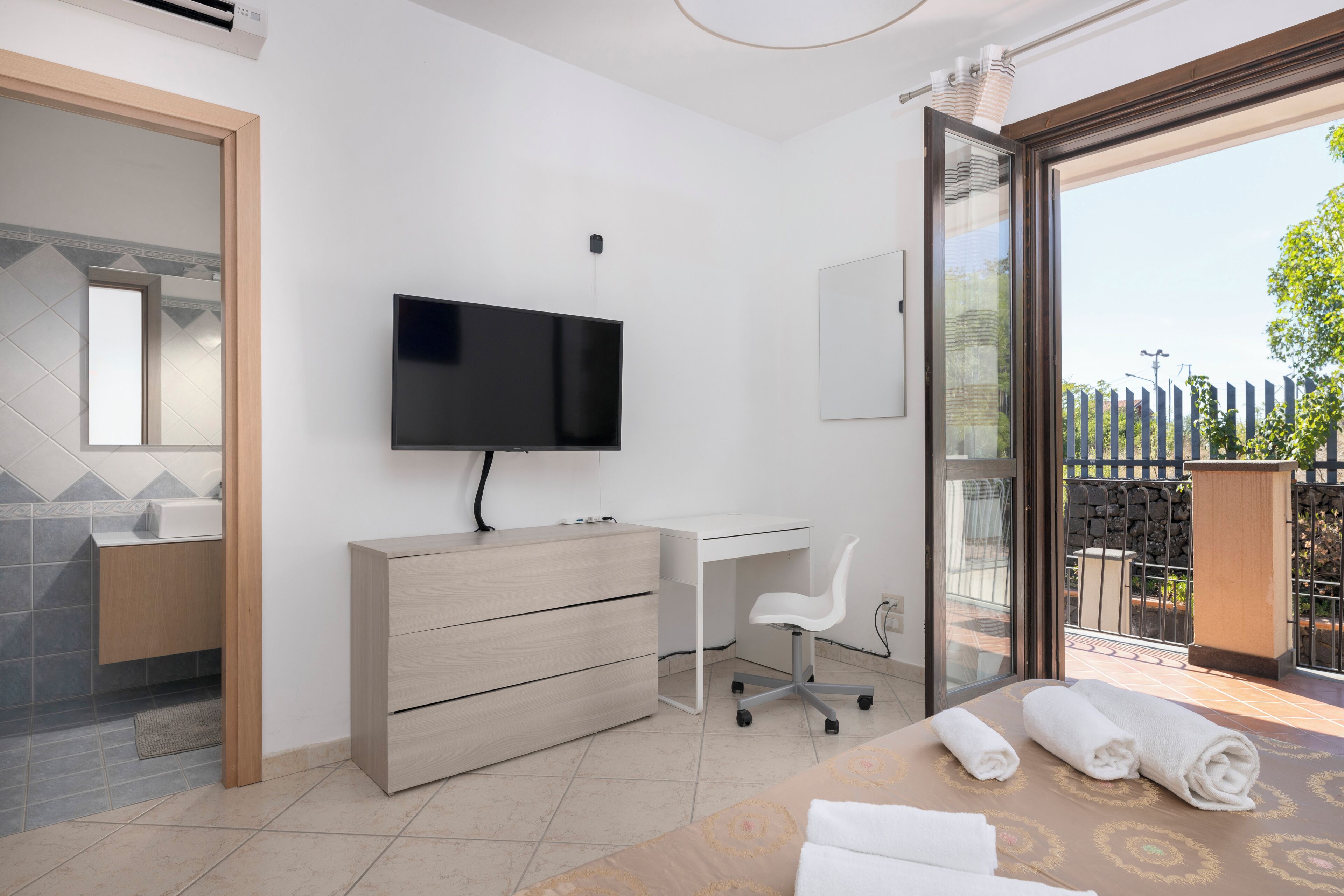A modern bedroom with a TV, desk, chair, and a balcony with a view.