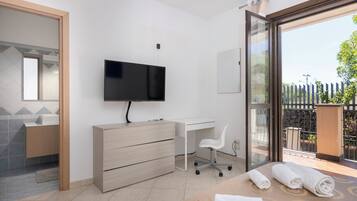 A modern bedroom with a TV, desk, chair, and a balcony with a view.