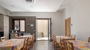 Un comedor con dos mesas, sillas, una cocina y un ventanal corredizo que da a un balcón.