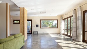 Una habitación amplia con un sofá verde, ventanas grandes y vistas a zonas verdes.