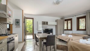 Una habitación de hotel moderna con kitchenette, zona de comedor, sofá cama y ventanas amplias.