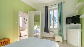 Un dormitorio con cama, televisor, armario y ventana con cortinas.