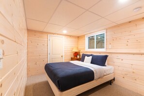 Un dormitorio acogedor con piso de madera, una cama con colcha azul y blanca, una mesita de noche con lámpara y una ventana con vistas al exterior.