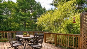 A wooden deck with a table and chairs, surrounded by a wooden fence and trees. - FAMILY-FRIENDLY, King Bed, Outdoor Space, Pet-Welcome - Intervale Lodge (Intervale)