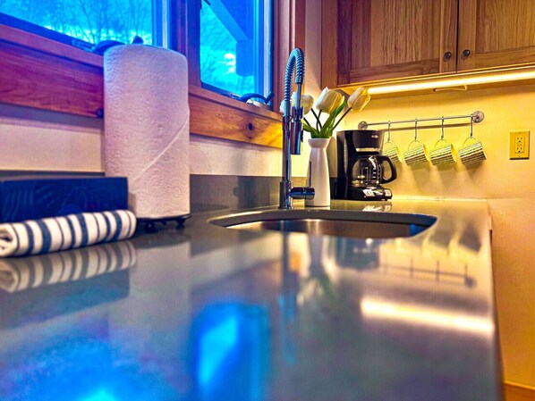 A kitchen with a stainless steel sink, a towel dispenser, and a coffee machine.