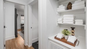 A hallway with a white wall, a wooden floor, and a shelf with folded towels and a potted plant. - Renovated Midtown Home, Walkers Dream  to Food/Fun (Reno)