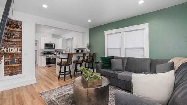 A modern living room with a grey sofa, a round coffee table with a plant, and a kitchen in the background. - Renovated Midtown Home, Walkers Dream  to Food/Fun (Reno)