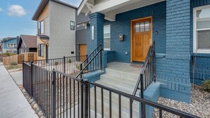 A modern two-story house with a blue brick exterior, a wooden front door, and a black metal staircase leading to the front porch. - Renovated Midtown Home, Walkers Dream  to Food/Fun (Reno)