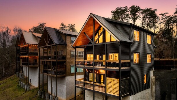 A multi-story log cabin with a balcony and large windows, surrounded by trees. - Lux Home-2 Master Suites-Heated Pool-Dollywood 5mi (Pigeon Forge)