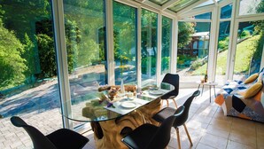 A conservatory with a glass table surrounded by chairs, a wooden coffee table, and a sofa with cushions. - Rustic Authentic Holiday Home with Terrace and Wood Stove - Three Bedroom Holiday Home with Terrace (Ljubno ob Savinji)