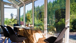 A conservatory with a glass table and chairs, surrounded by large windows offering a view of a forested area. - Rustic Authentic Holiday Home with Terrace and Wood Stove - Three Bedroom Holiday Home with Terrace (Ljubno ob Savinji)