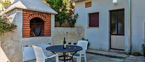 A stone oven, a table with chairs, and a building with a door and window.