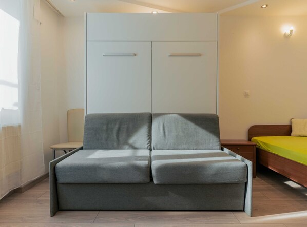 A modern room with a grey sofa, a bed with a yellow bedspread, and a wardrobe with two doors. - Ljubljana City Charming Apartment - Studio Apartment (Ljubljana)
