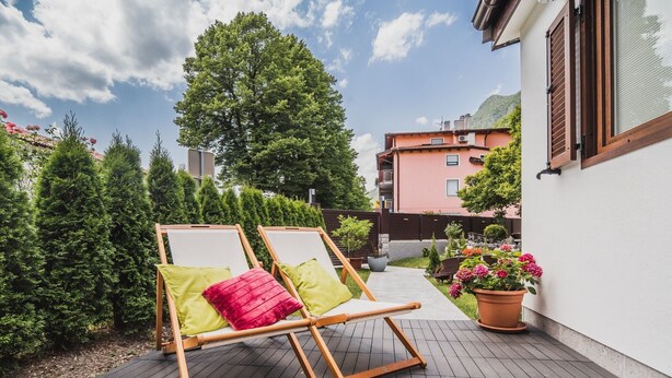 Un terrazzo in legno con due poltrone prendisole, una pianta in vaso e un edificio sullo sfondo.