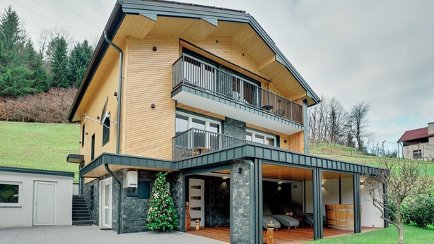 A modern two-story house with a balcony, a stone fireplace, and a wooden deck.