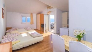Quarto com cama, escrivaninha e cadeira. Há uma janela e uma porta que dá para uma varanda.