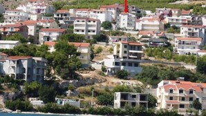 Uma área residencial costeira com edifícios de vários andares, alguns com varandas, e uma colina ao fundo.