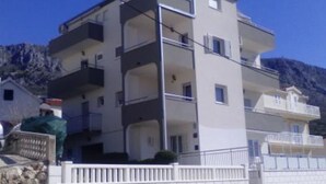 Um edifício residencial de vários andares, com varandas, uma parede de pedra em frente e montanhas ao fundo.