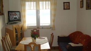 Uma área de refeições com uma mesa, cadeiras, uma televisão e uma janela com cortinas.