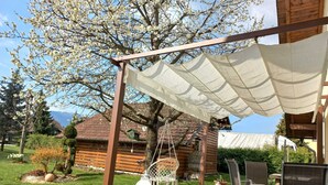 Une cabane en bois dotée d’un patio couvert, de meubles d’extérieur et d’un jardin agrémenté d’arbres en fleurs.