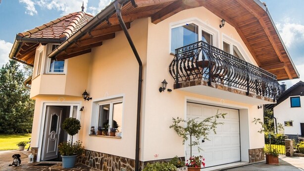 Une maison à deux étages avec un toit en pente, un balcon doté d’une balustrade en fer forgé et une porte de garage.